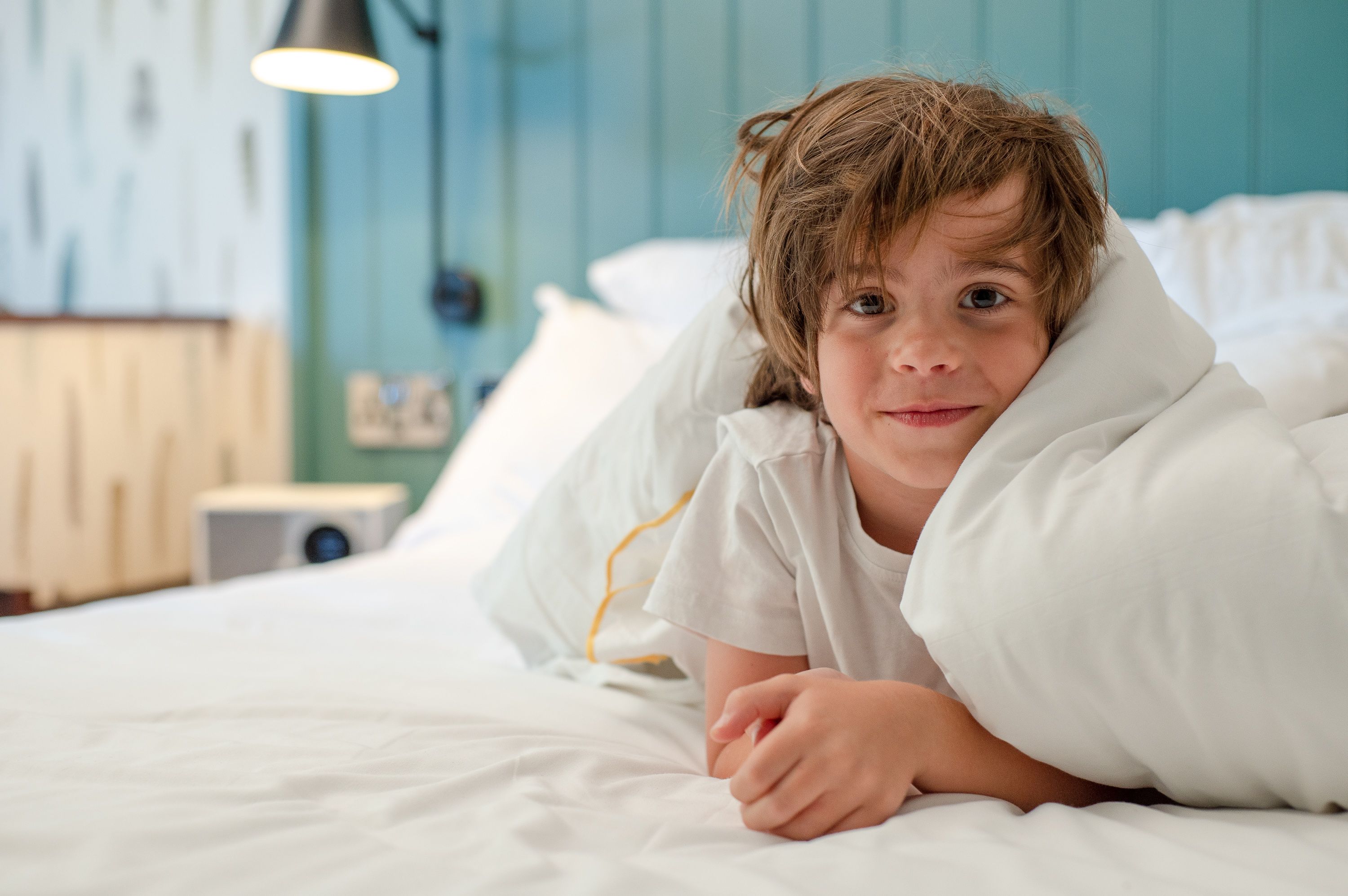 A young boy under the covers looking at the camera